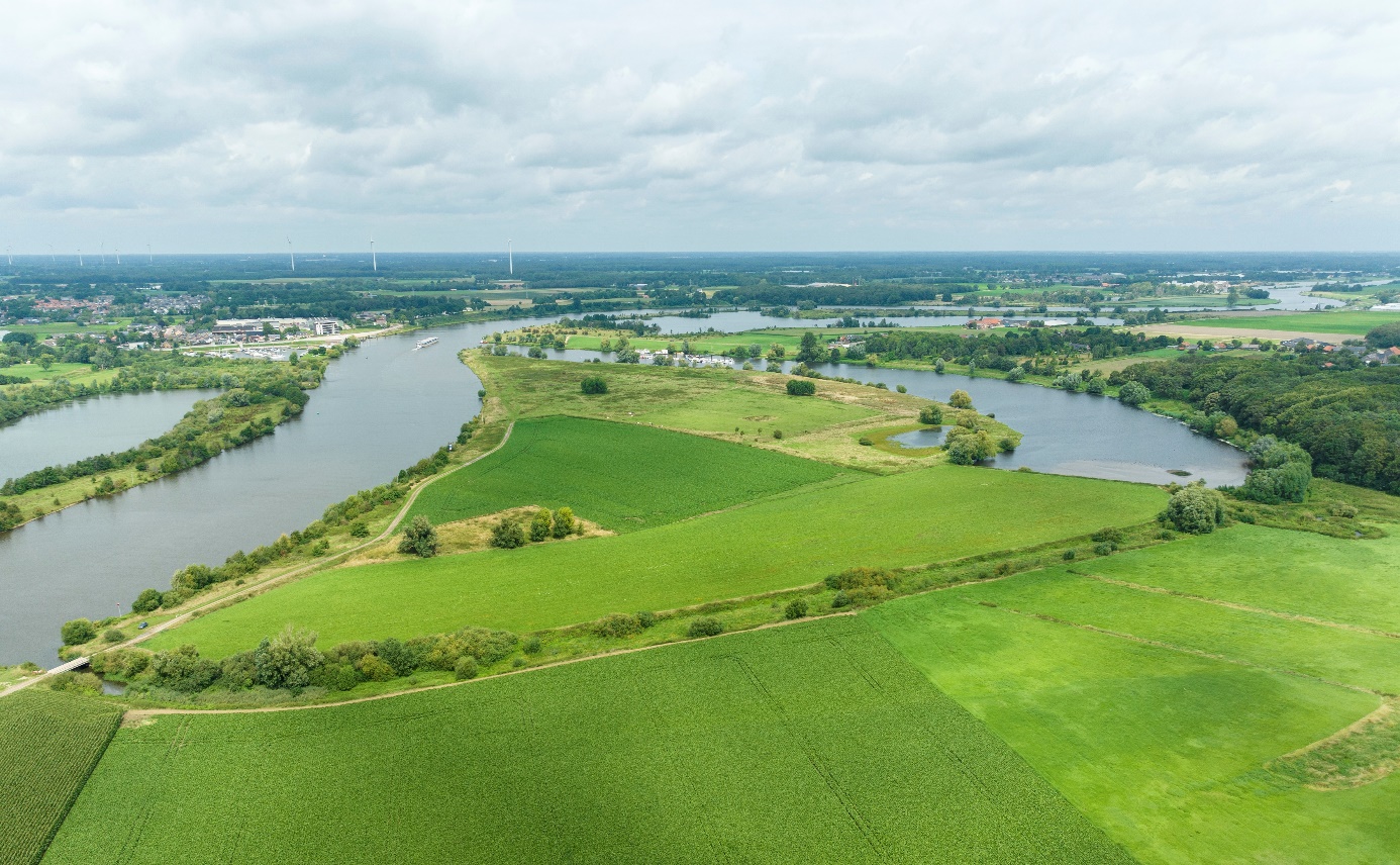 Foto van Geul Hansummerweerd-Oude Maasarm met onderin de foto een groot groen landschap met boven blauw water wat het land omarmt.